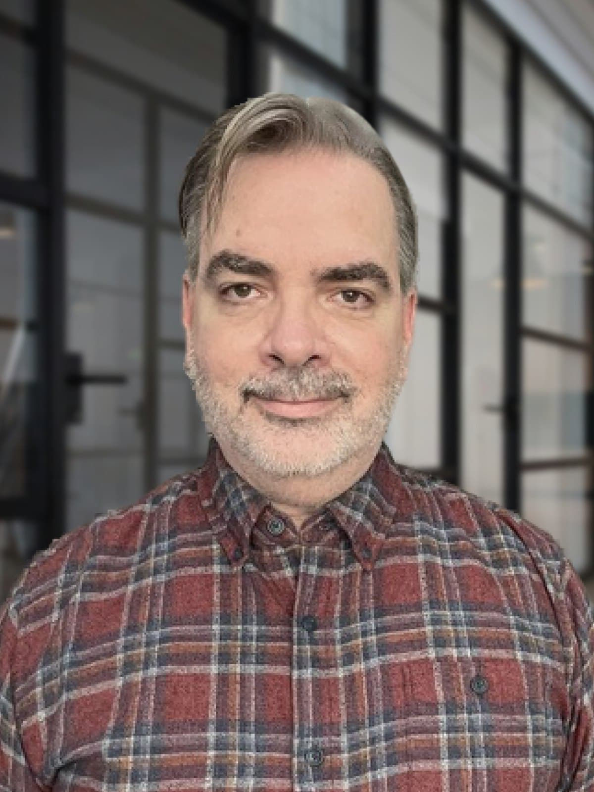 Alfonso Barreiro, Product Designer, in a plaid shirt in an office hallway.